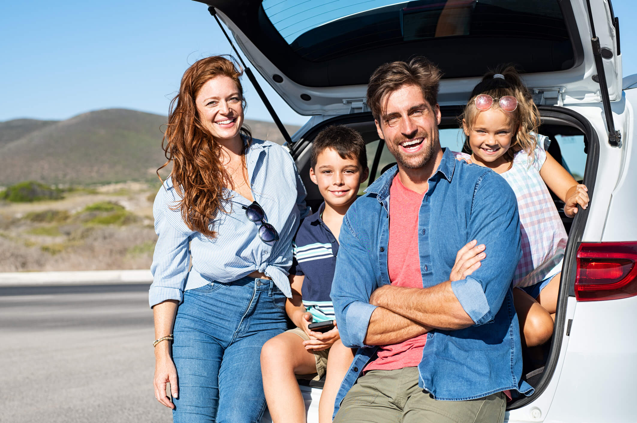 a mom, dad, and two young kids leans against their minivan